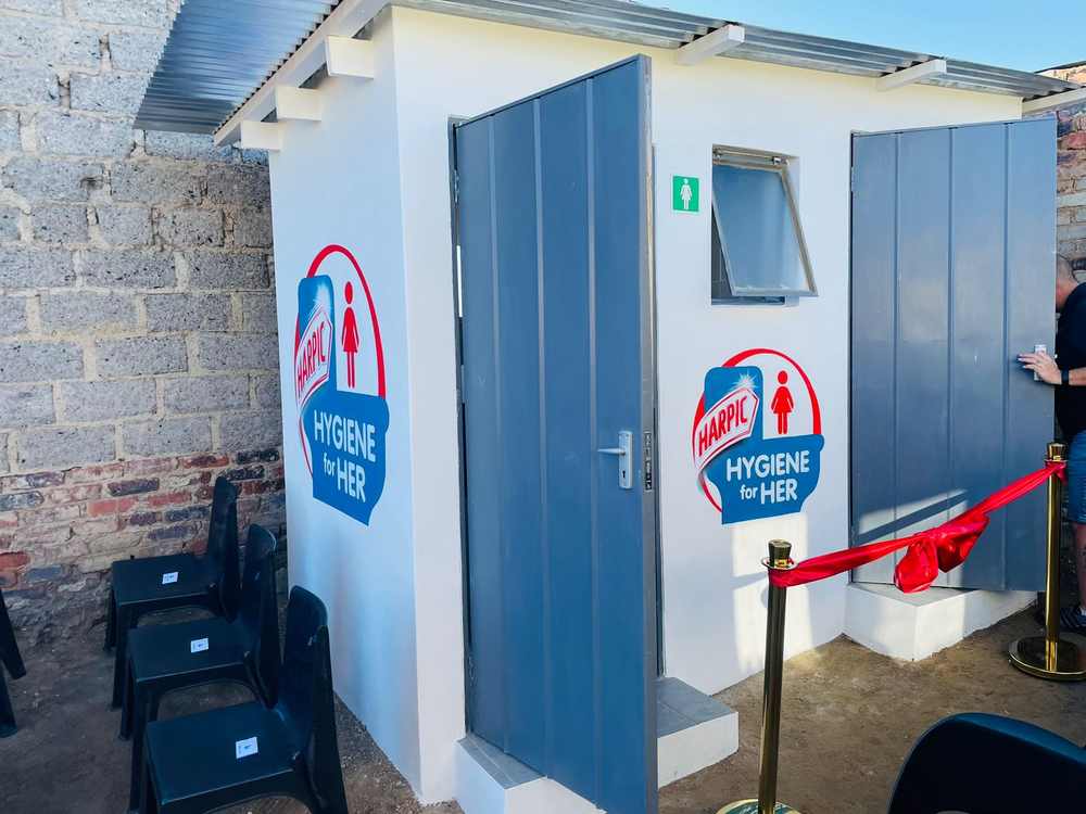 Newly built women-only sanitation facility painted white with Harpic Hygiene for Her branding, red ribbon ready for opening