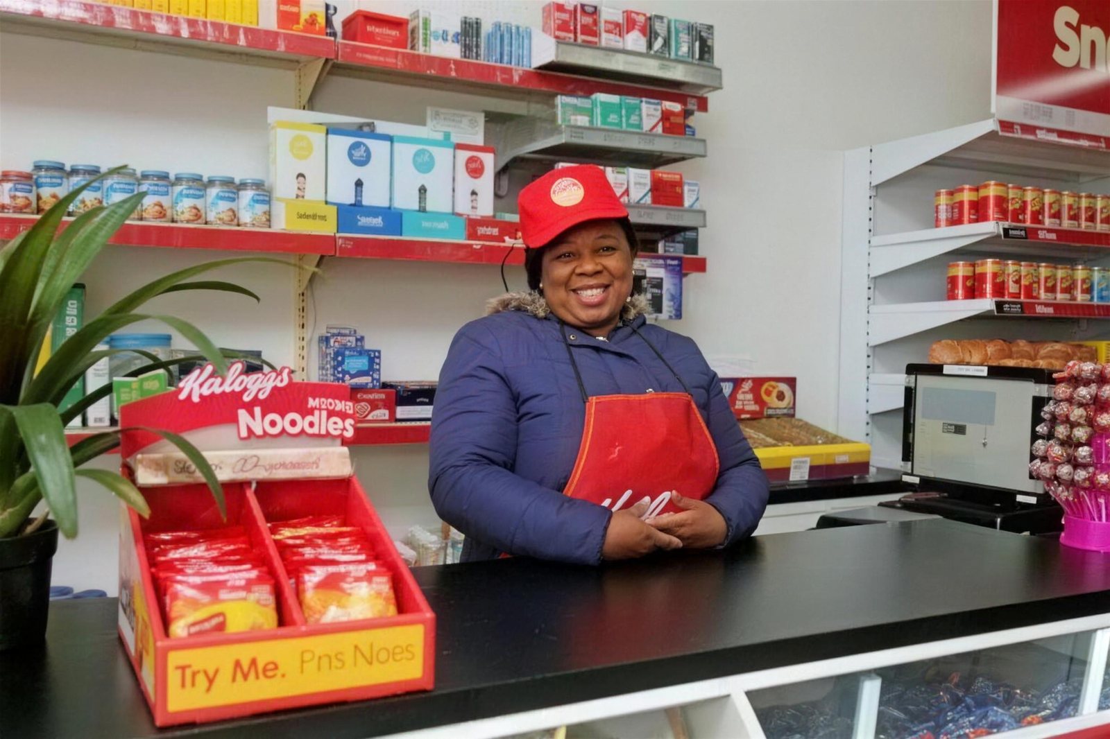 Store owner smiling behind the counter of her rebuilt Kellogg's branded spaza store
