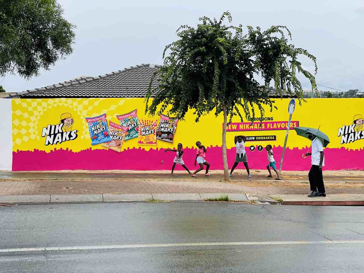 Children playing on the pavement in front of a yellow and magenta NikNaks wall mural