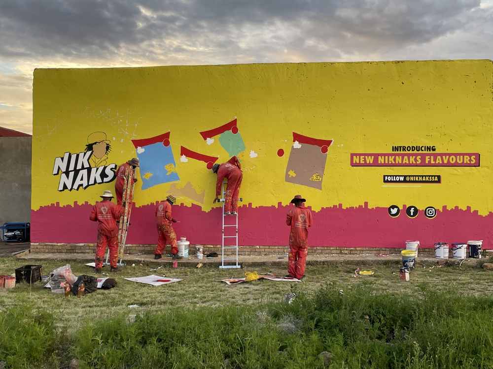 Cornerhouse artist team painting a NikNaks wall mural from ladders
